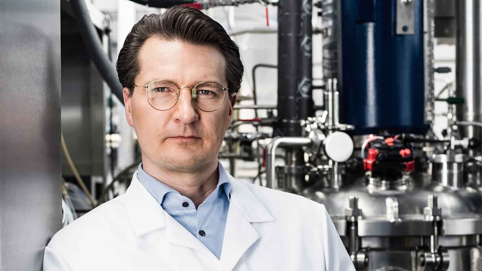 Man in a labcoat standing in front of machinery